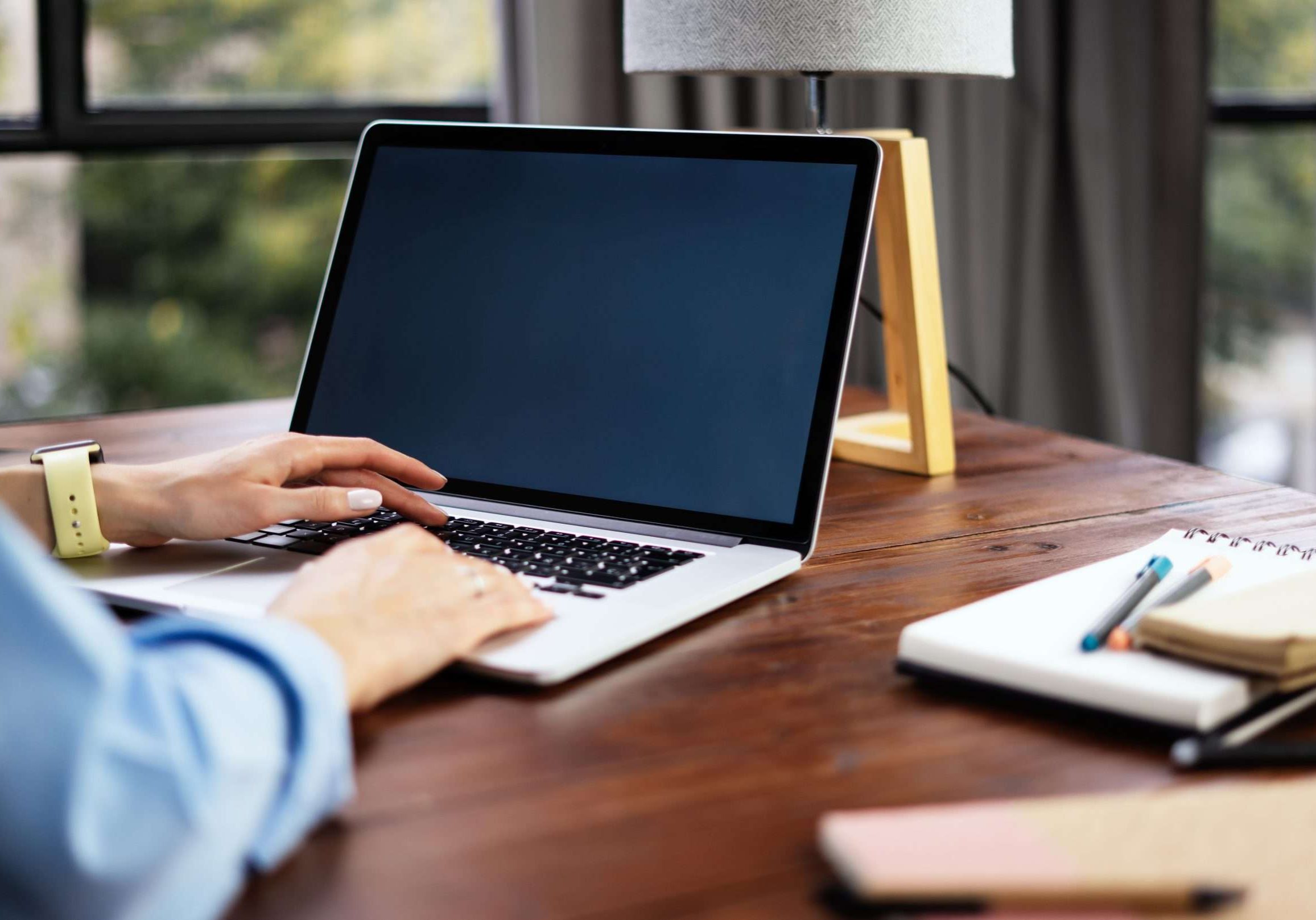 Mockup image of a woman using laptop with blank screen on wooden table. Female writer keyboarding on computer while working on her new article